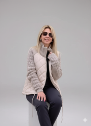 Woman modeling quilted beige puffer vest with gray knitted sweater sleeves. Ideal for winter online store.